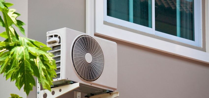 Outdoor air conditioning unit mounted beside a home’s window.