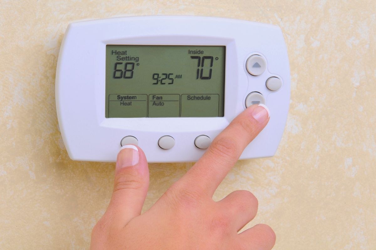 A homeowner adjusting a thermostat with the fan set to AUTO for heating.