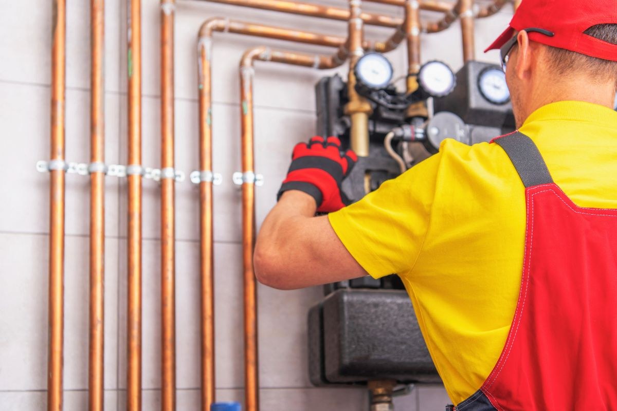 Furnace maintenance performed by a technician in red overalls working on a boiler with copper pipes