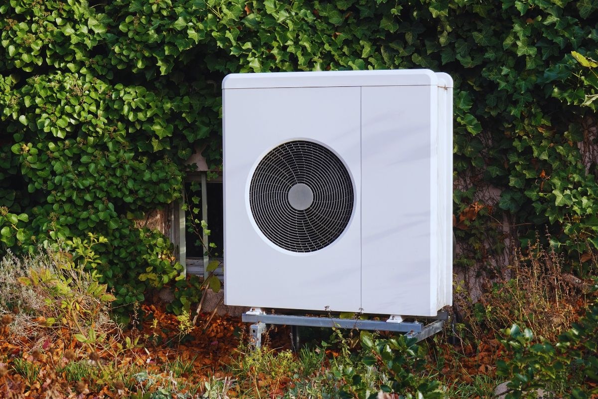 Modern outdoor heat pump unit installed against a green ivy-covered wall, typical of home heating systems needing heater repair or maintenance