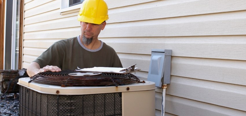 Technician inspecting an outdoor AC unit as part of learning how to unclog ac drain line.