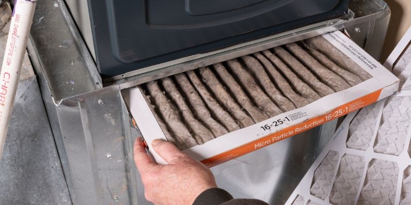 Technician removing a pleated air filter from a ventilation unit, showing one of the common hvac filter types used in HVAC systems.