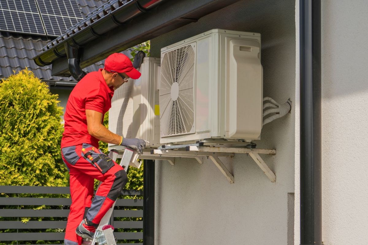 Professional technician performing an HVAC tune up on an outdoor AC condenser unit from a ladder.