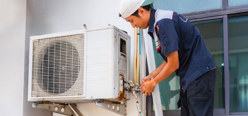 HVAC technician repairing the outdoor AC condenser unit, often needed when the house feels humid with ac running