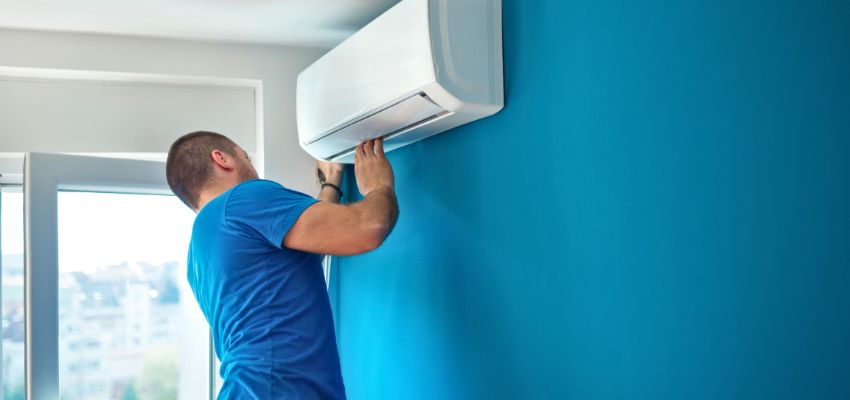 Man servicing a wall-mounted air conditioner, a common issue when the house feels humid with ac running