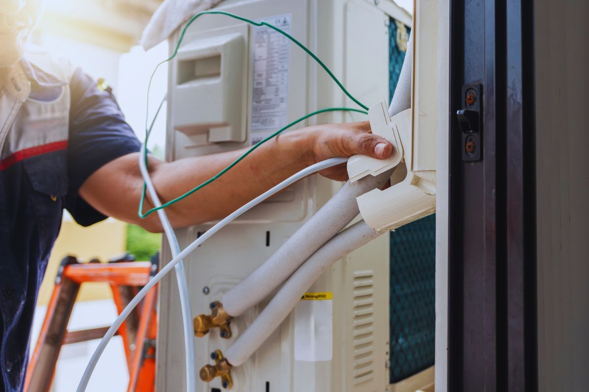 Skilled installer carefully routing and securing insulated refrigerant lines and condensate drain during the hvac rough in phase of a new air conditioning system setup