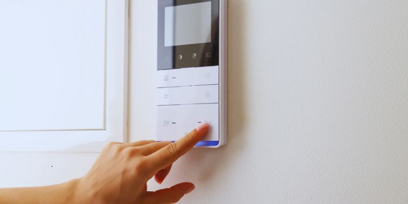 Person's finger pressing a button on a modern wall-mounted thermostat control panel with digital display, demonstrating user interface for an HVAC zoning system in a home.