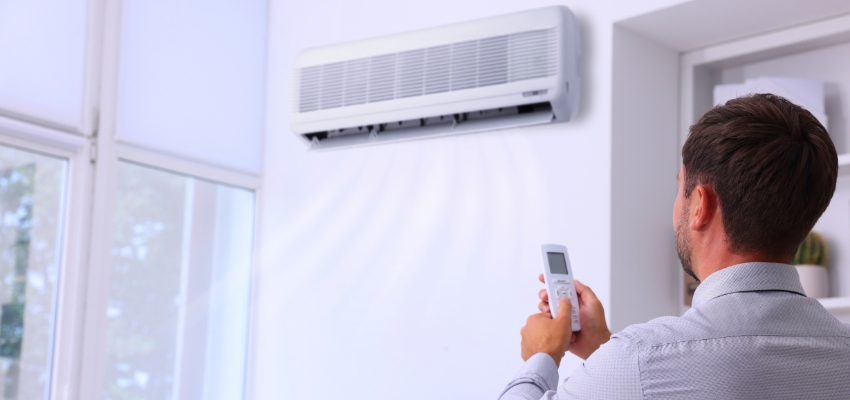 Man adjusting temperature with remote for his Freon AC system in a living room.