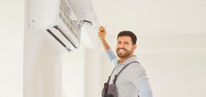 Smiling technician performing maintenance on a mini split unit, highlighting reliability factors in whether are mini splits worth it.