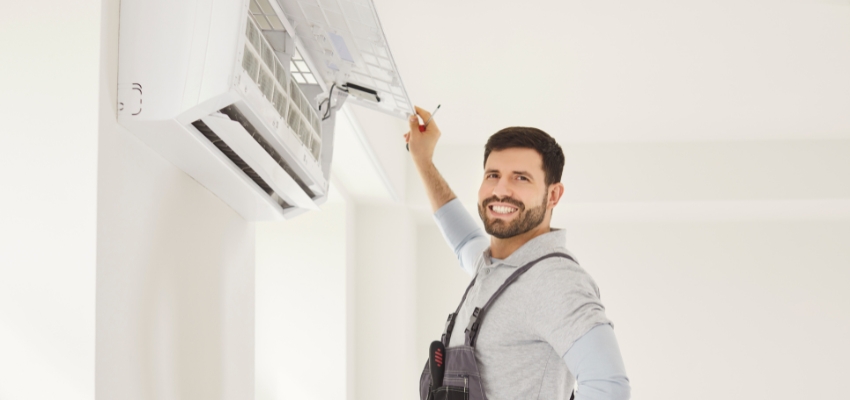 Smiling technician servicing one of the efficient wall air conditioners