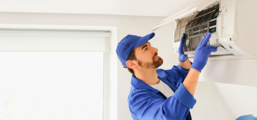 Technician inspecting a wall AC unit to diagnose a possible ac refrigerant leak.