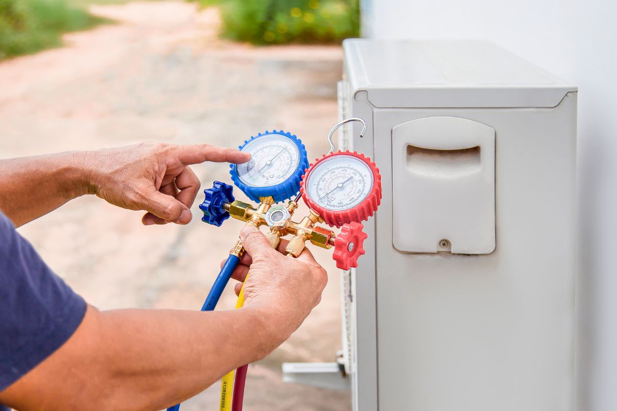 Technician using pressure gauges on an outdoor unit to detect an ac refrigerant leak.