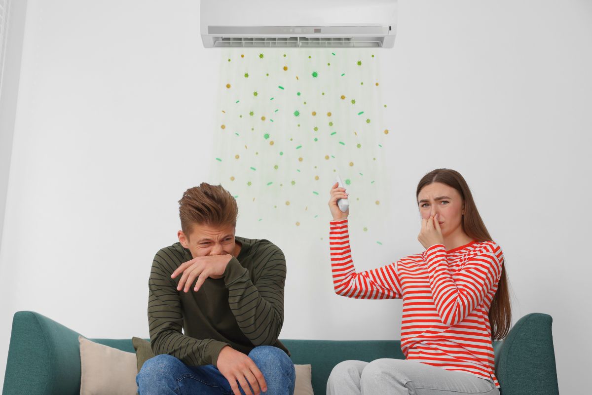 Couple reacting to musty air from an AC unit, a classic sign of dirty sock syndrome.