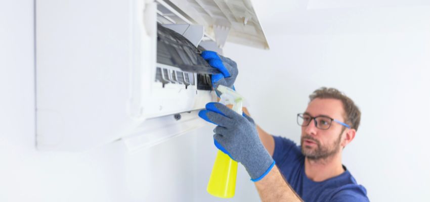 Technician cleaning an AC unit to eliminate the causes of dirty sock syndrome.