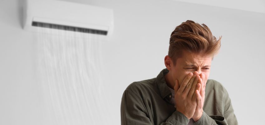 Man covering his nose near a wall unit due to the odor of dirty sock syndrome.