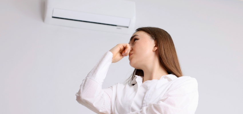 Woman covering her nose near a wall unit due to possible mold in air conditioner.